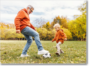 A father and son play soccer on lawn in the park.